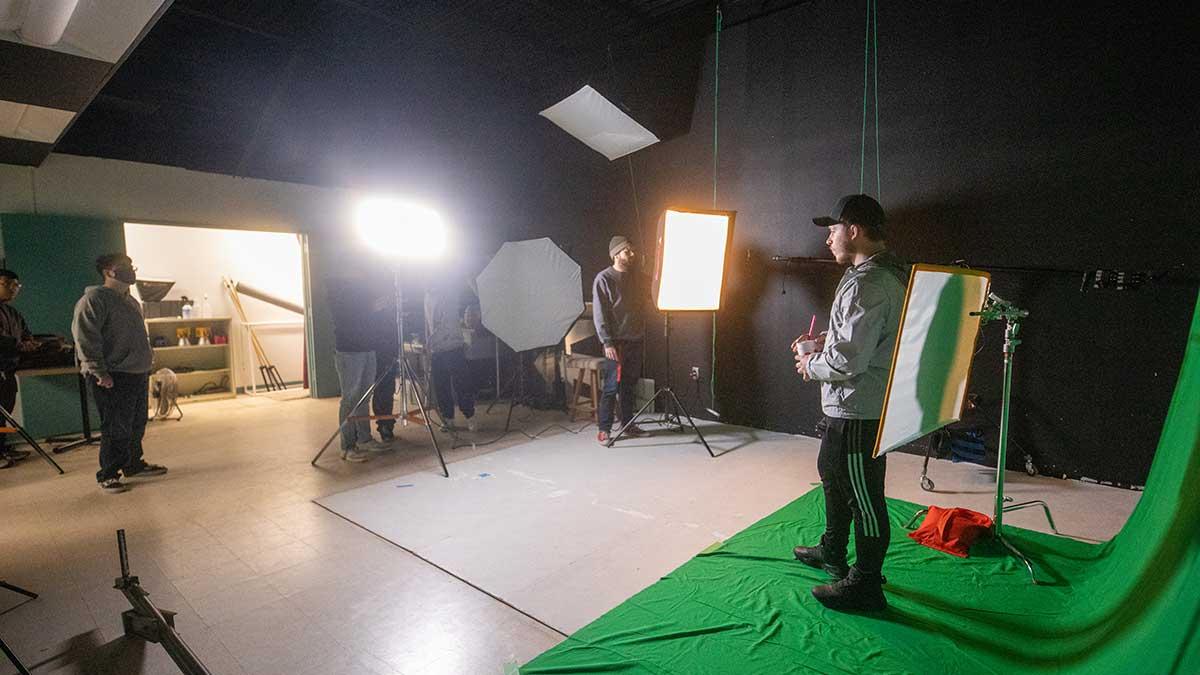 Students standing in front of a green screen with film equipment.